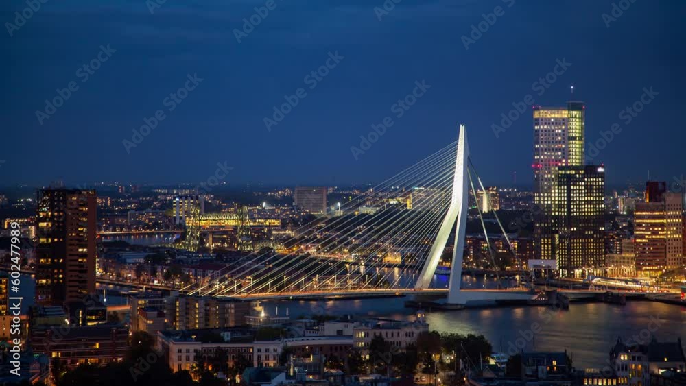 A beautiful timelapse of Rotterdam's skyline and Erasmus Bridge in the Netherlands. This autumn evening showcases a cloudy atmosphere as the city lights illuminate the scene.