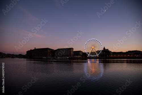 Nightly view of a spinning ferris wheel in Toulouse, landscape river and buildings