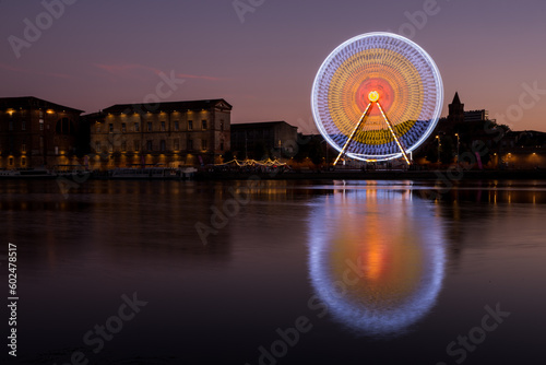 Panoramic view of the banks of the Garonne River at night with the illuminated Ferris wheel in motion.