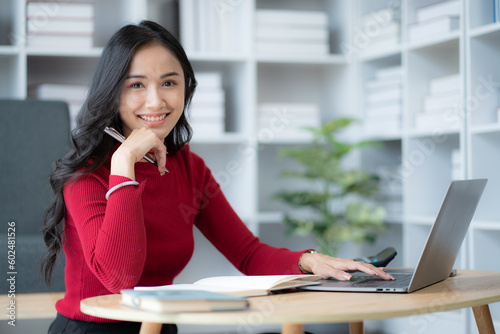 beautiful Asian girl wearing red sweater working with laptop computer in the living room.