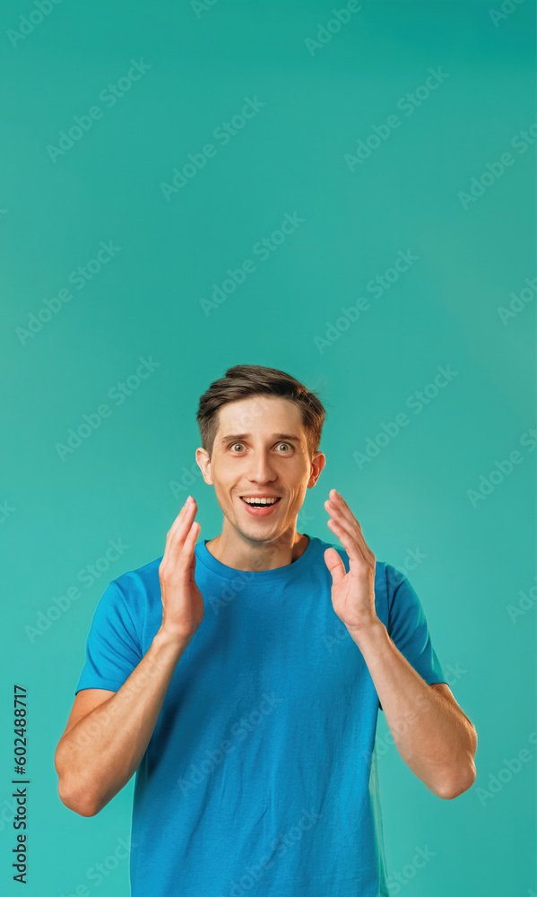 Surprised man. Expressive emotion. Astonished optimistic handsome guy in blue raised arms looking big amazed eyes isolated on turquoise copy space background. Surprised man. Expressive emotion. Astonished optimistic handsome guy in blue raised arms looking big amazed eyes isolated on turquoise copy space background.