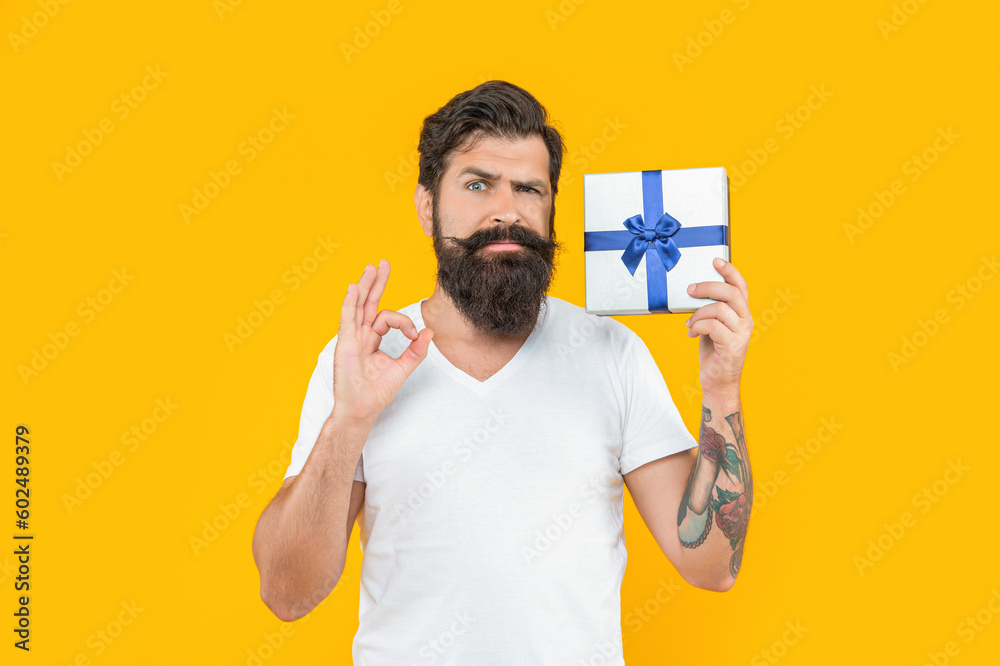 serious bearded man hold present box isolated on yellow. bearded man hold present box in studio serious bearded man hold present box isolated on yellow. bearded man hold present box in studio