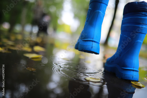 legs of child in blue rubber boots jumping in the autumn puddles