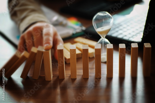 domino effect concept with wooden tiles blocked by hourglass with background photo