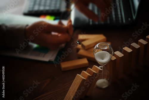 domino effect concept with wooden tiles blocked by hourglass with background