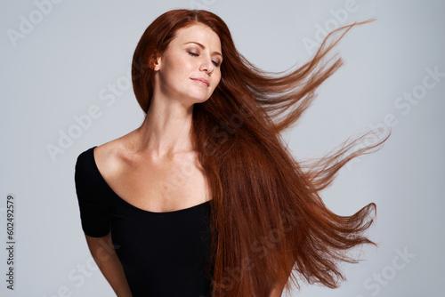 Hair, beauty and woman in studio with wind for keratin treatment, wellness and haircare on gray background. Salon, hairdresser and face of ginger female model for shine, healthy and natural hairstyle photo