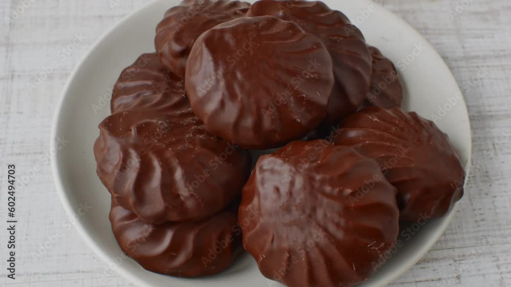 Chocolate marshmallows on a white saucer. Marshmallows in chocolate glaze close-up lying on a white glass plate. The concept of children's caries from candies and sweets Chocolate marshmallows on a white saucer. Marshmallows in chocolate glaze close-up lying on a white glass plate. The concept of children's caries from candies and sweets