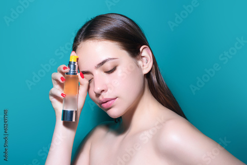 Young pretty woman smelling perfume. Sensual woman with bottle of perfume, beauty portrait. Female perfume, fragrance. Girl holding up bottle of perfumery. Luxury perfume. Adv for perfumes store.