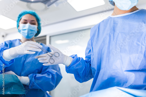 Low Angle Shot in the Operating Room, Assistant Hands out Instruments to Surgeons During Operation. Surgeons Perform Operation. Professional Medical Doctors Performing Surgery.