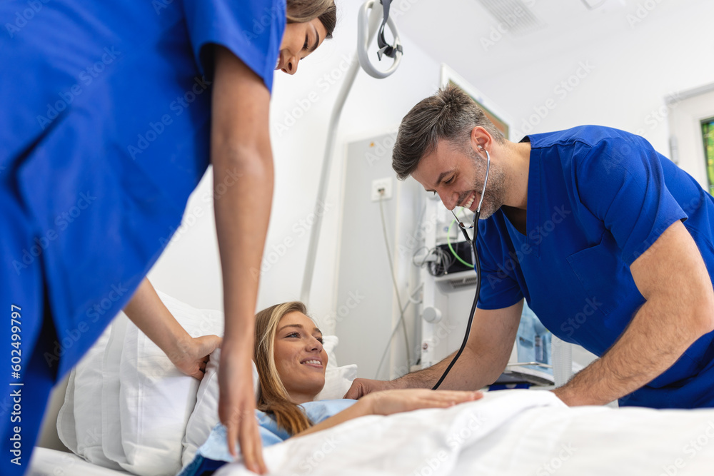 Obraz premium Hospital Ward Friendly Doctor and nurse taking care of Beautiful Caucasian Female Patient Resting in Bed. Physician explains Test Results. Woman Recovering after Successful Surgery