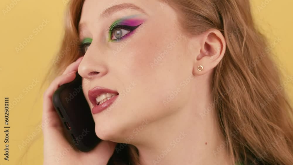 View of a young red-haired woman talking on the phone. A woman stands on an orange background and argues with someone on the phone. View of a young red-haired woman talking on the phone. A woman stands on an orange background and argues with someone on the phone.