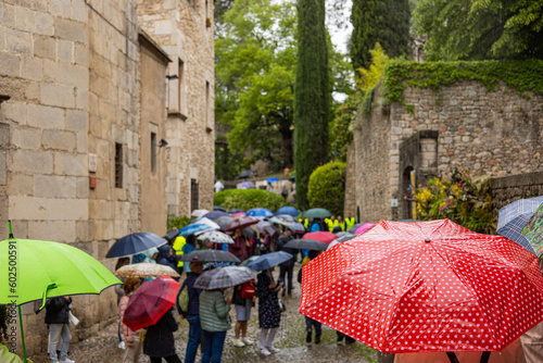 Fototapeta Naklejka Na Ścianę i Meble -  Girona, Spain - May 13th, 2023: TEMPS DE FLORS - Flower Time. Crowd of tourists walking with umbrellas through Old Town on a rainy day through Archaeological Park, Cathedral Gardens and Arab Baths..