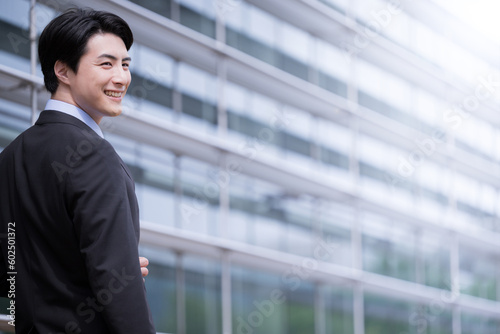 Mid-career or career change image Male employee in his 30s with black hair wearing a jacket and a smile in front of an office building Copy space