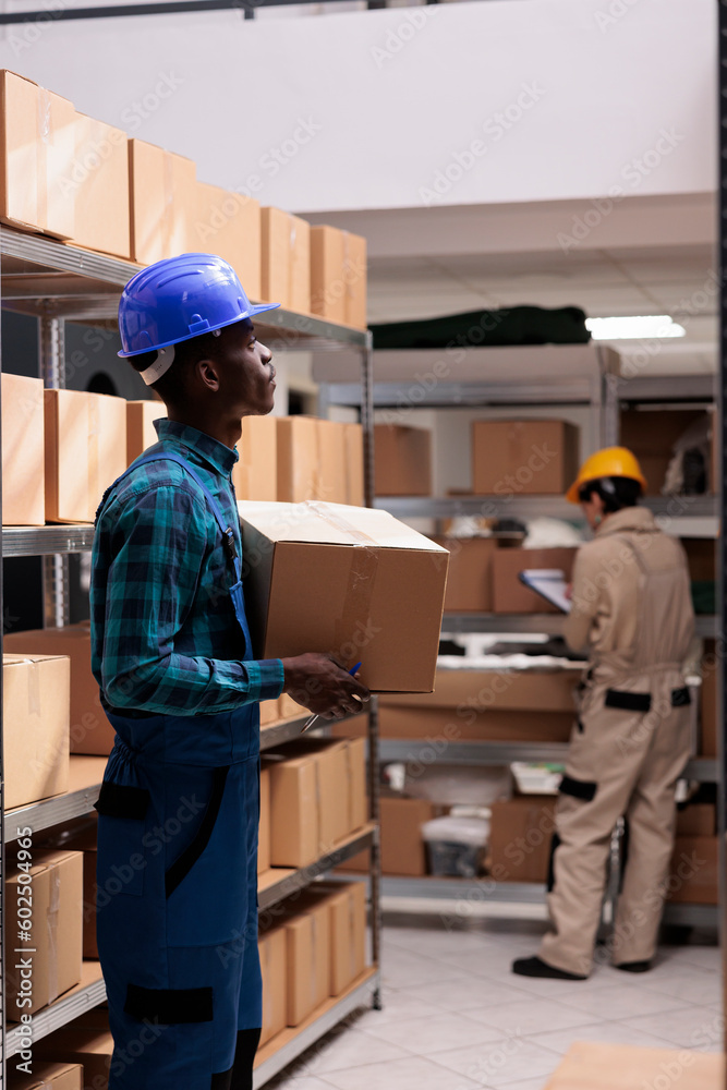 Mail sorting center worker holding packed cardboard box with client order. Shipping company african american man employee carrying carton and managing parcels transportation Mail sorting center worker holding packed cardboard box with client order. Shipping company african american man employee carrying carton and managing parcels transportation