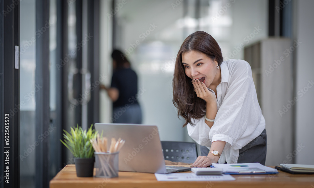 Excited Happy Asian young woman using phone and laptop sitting on a desk office in the day at office Excited Happy Asian young woman using phone and laptop sitting on a desk office in the day at office