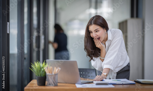 Excited Happy Asian young woman using phone and laptop sitting on a desk office in the day at office 