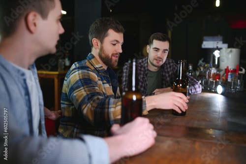 Friends having fun. Happy young men in casual wear drinking beer in pub.