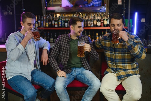 Young men in casual clothes are talking  laughing and drinking while sitting at bar counter in pub
