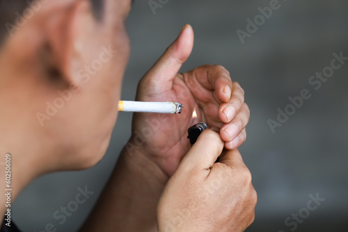 asian man lights cigarette in his mouth using a lighter