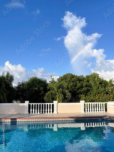Small piece of rainbow over the tropical garden with swimming pool.