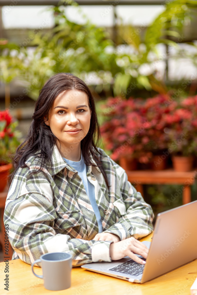 Fototapeta premium Portrait of a female florist typing on a laptop at a table in a flower shop.