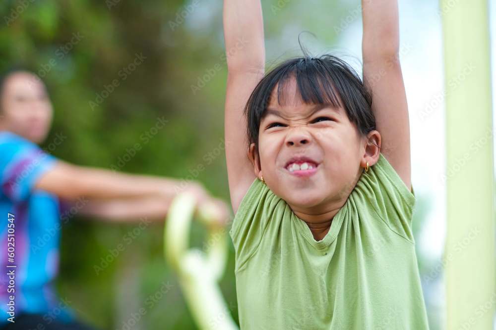 Little girl hanging on the horizontal bar on the playground. Cute young Asian girl hangs bar by hand to exercise at outdoor playground. Little girl hanging on the horizontal bar on the playground. Cute young Asian girl hangs bar by hand to exercise at outdoor playground.