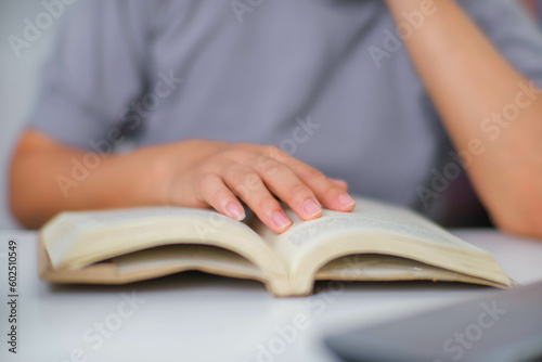 Closeup image of Asian woman sitting at a table reading a book in the living room.