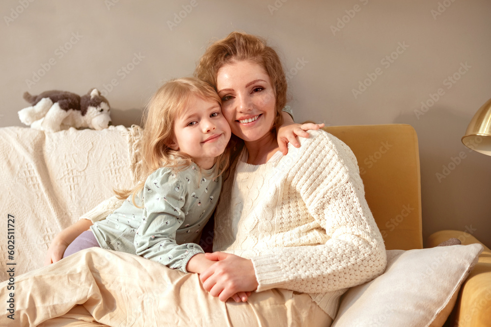 Mother and daughter sitting together on the couch in the room and cuddling