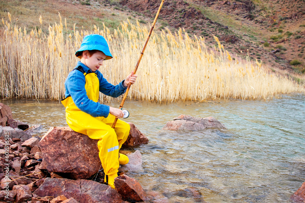 a little fisherman boy with a fishing rod in a yellow fishing jumpsuit a little fisherman boy with a fishing rod in a yellow fishing jumpsuit