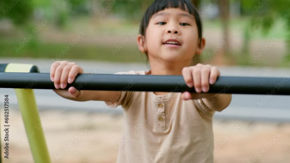 Little girl hanging on the horizontal bar on the playground. Cute young Asian girl hangs bar by hand to exercise at outdoor playground. Little girl hanging on the horizontal bar on the playground. Cute young Asian girl hangs bar by hand to exercise at outdoor playground.
