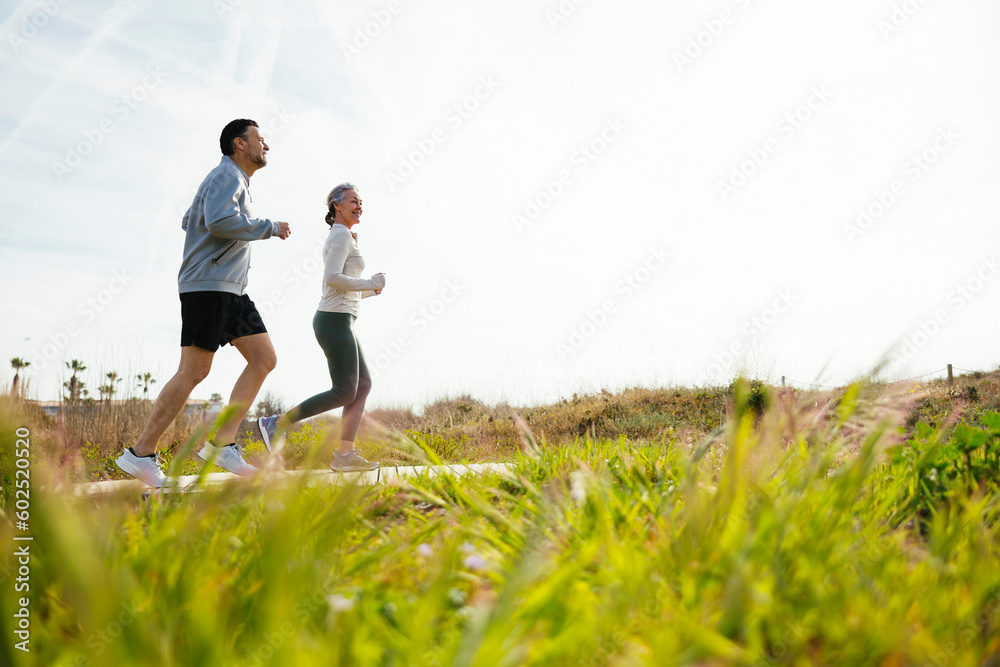 Mature couple running on boardwalk at grassy beach Mature couple running on boardwalk at grassy beach