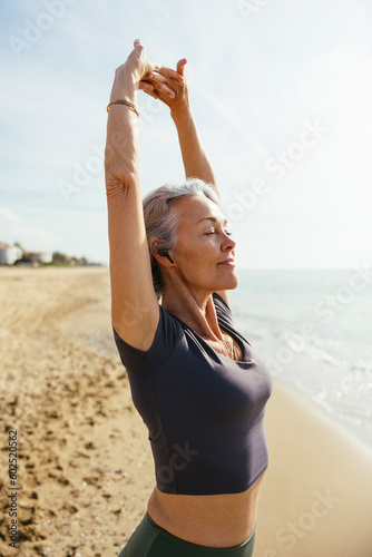 Mature woman stretching with eyes closed at beach