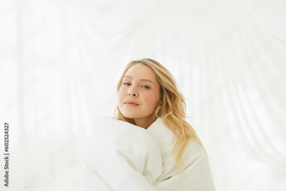 Woman with blond hair wrapped in white blanket by translucent curtain Woman with blond hair wrapped in white blanket by translucent curtain