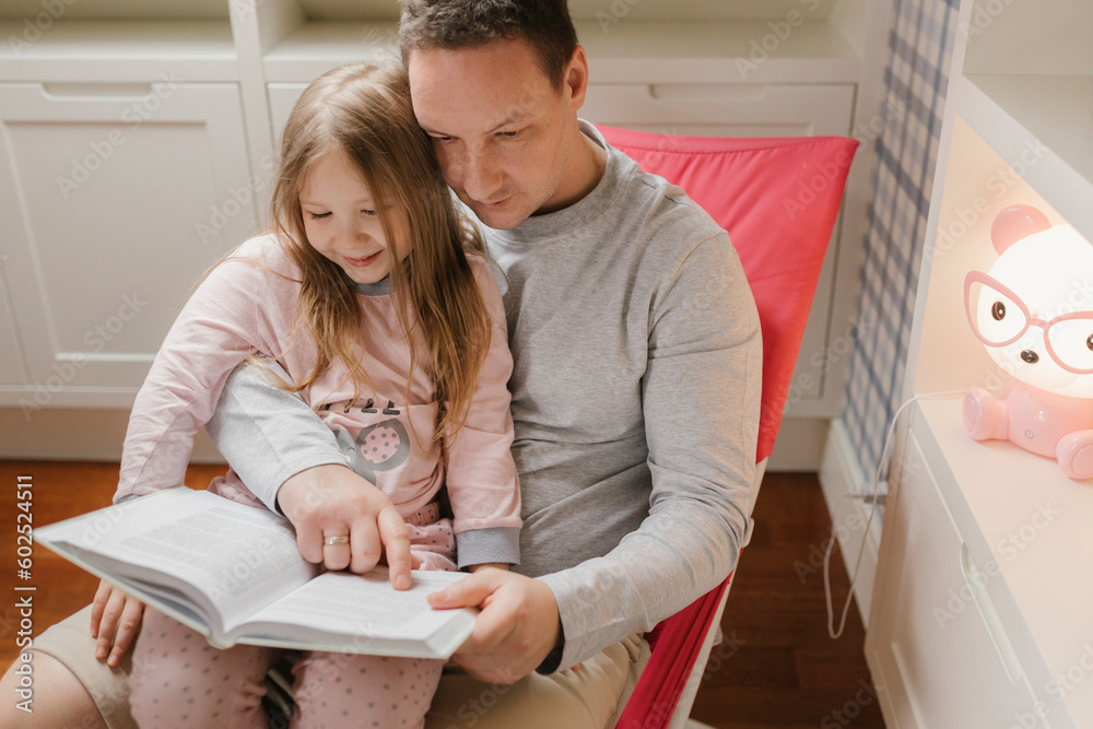 Girl sitting with father reading book at home Girl sitting with father reading book at home