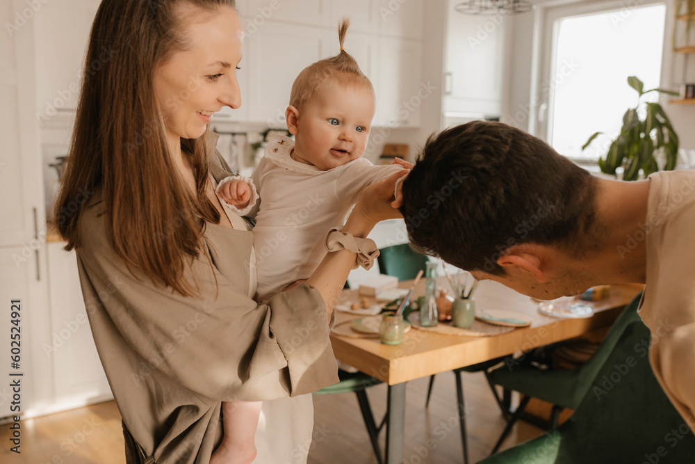 Happy woman carrying playful daughter touching hair of man at home Happy woman carrying playful daughter touching hair of man at home
