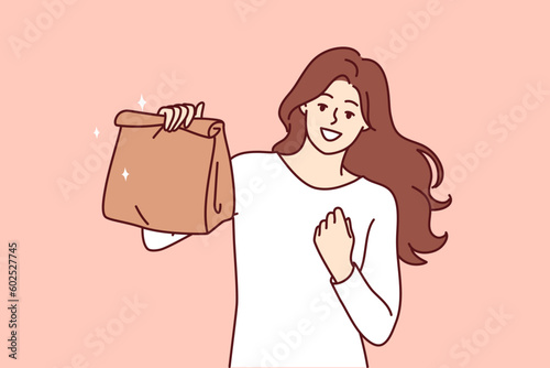 Woman with paper bag making victory gesture demonstrating food ordered from restaurant with delivery. Takeaway package for food or drinks in hand of girl delighted with purchase of delicious lunch
