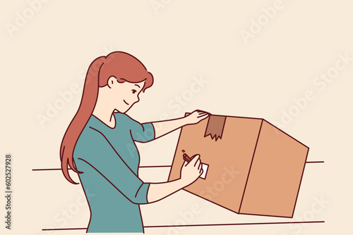 Woman with cardboard box signs package before sending goods through postal service or courier company. Young girl with big box packs household items when moving or renovating apartment