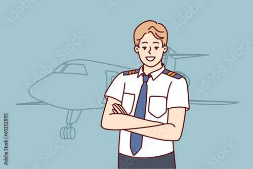 Man pilot of airplane stands with arms crossed near airliner inviting to buy new airline ticket. Confident guy airliner captain or aircraft pilot posing before departure from airport