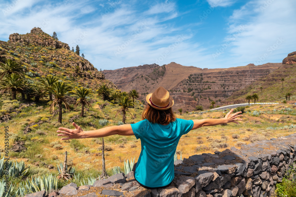 A young tourist with a hat sitting on the viewpoint of El Palmarejo in La Gomera, Canary Islands