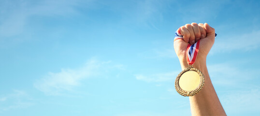 Gold medal held in athlete hand raised against sky background