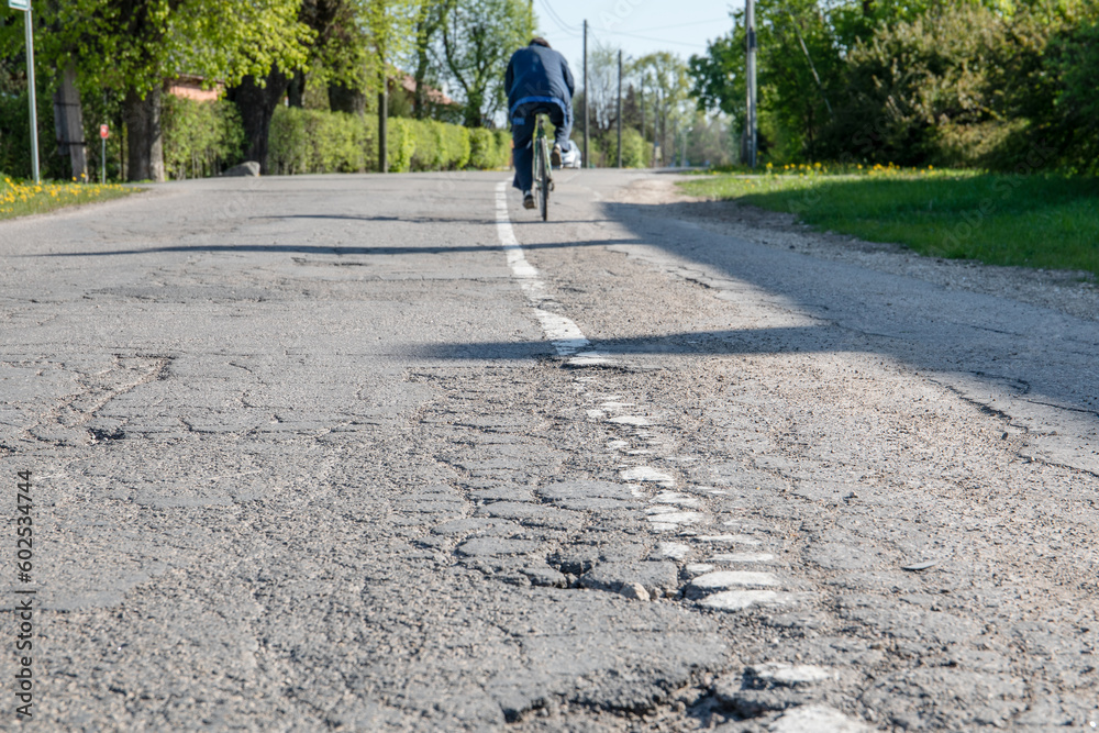Damaged asphalt road. A cyclist in the background