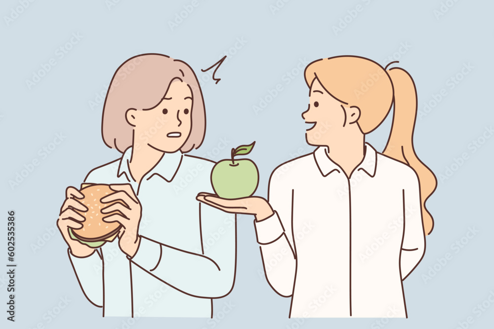 Woman nutritionist offers apple to girl who eats fast food with high content of cholesterol and fat