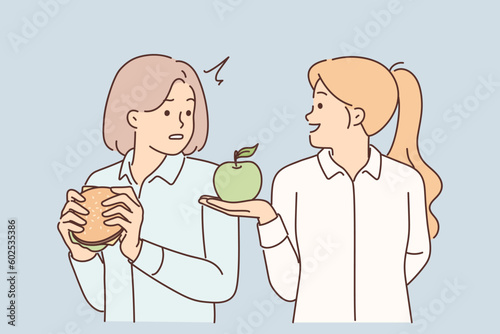 Woman nutritionist offers apple to girl who eats fast food with high content of cholesterol and fat