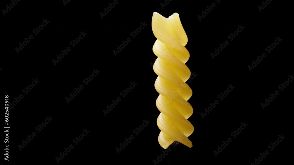 spiral pasta fusilli, or macaroni rotates on a black background moves and stops at the edge, close-up. spiral pasta fusilli, or macaroni rotates on a black background moves and stops at the edge, close-up.