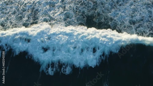 Aerial view of a wave following its path as it breaks, with surfers entering