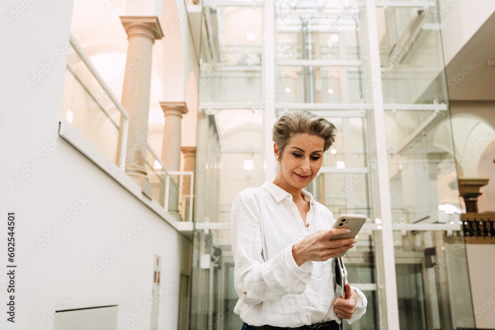 Portrait of woman art gallery manager using smartphone while standing in museum