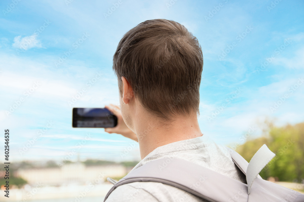 a man takes photos on his phone. A young man on the street takes a photo, a warm summer day. Travel and tourism. back view.