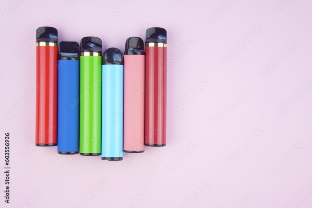 Set of multicolor disposable electronic cigarettes on a pink background.