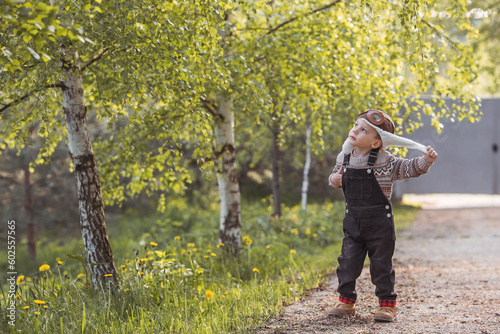 A little boy of 4 years old in an aviator cap and stylish clothes plays outdoors in spring. Portrait of a child on the background of a birch grove. © Юлия Клюева
