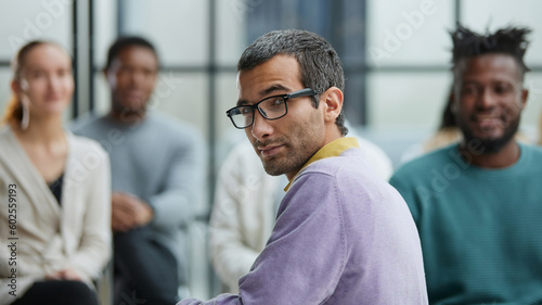 a man in casual clothes with glasses looks at the camera while sitting together with his colleagues